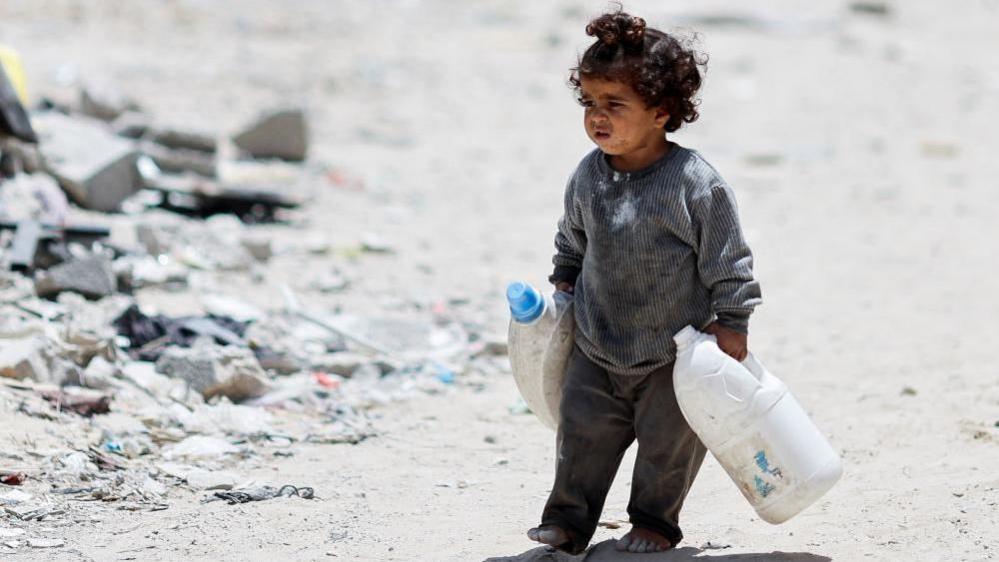 A Palestinian girl carries cans to collect water in Khan Younis, in the southern Gaza Strip, on 22 May