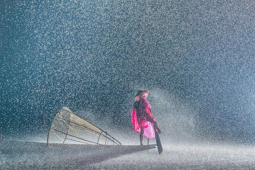 A fisherman in Myanmar perches on a boat fishing in heavy rain