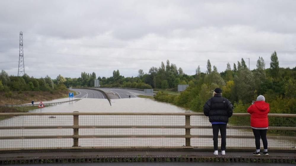 People look at flood water on the A421 in Marston Moretaine, Bedfordshire, 23 September