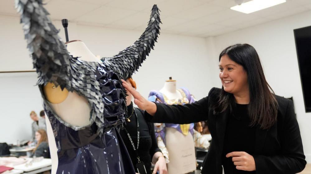 Culture Secretary Lisa Nandy, dressed all in black and smiling, inspects a fantasy-style costume with grey metallic horns on her visit to Pinewood Studios. 