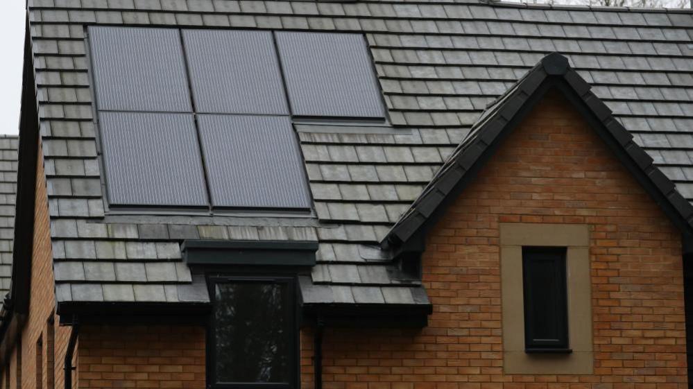 A brick house with a black roof with solar panels on it.