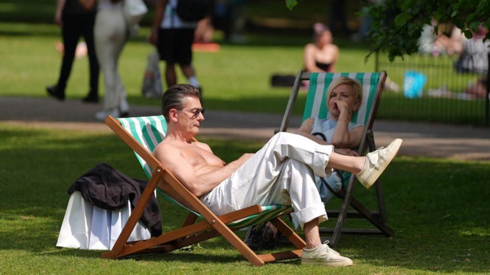 A shirtless man reclines on a beach chair in a park