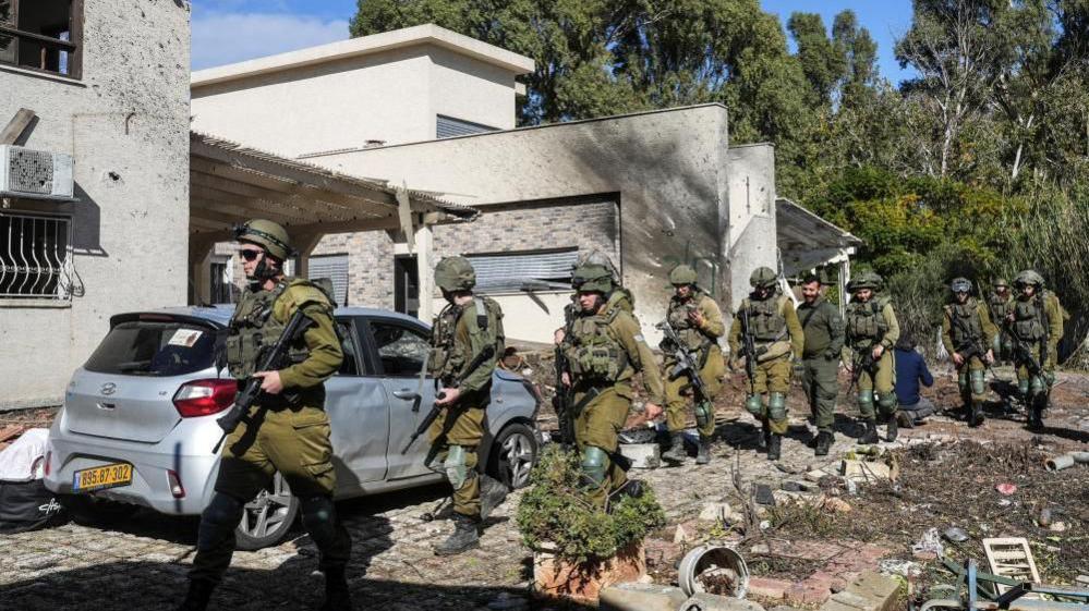 Israeli troops walk past a house damaged by rocket fire in Kiryat Shmona, 26 Nov