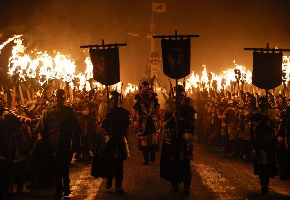 People in Viking outfits drag a boat behind them while carrying lit torches and shields