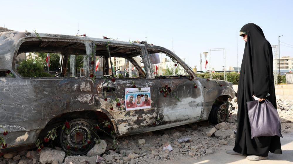 A veiled Iranian woman stands next to an ambulance of the Iranian Red Crescent Society (IRCS) that was destroyed in an Israeli strike, in Tehran, Iran, 23 June 2025.
