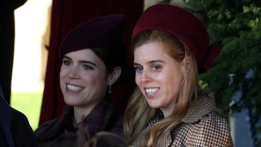 Princesses Beatrice and Eugenie at the Royal Family's Sandringham Christmas service. Eugenie wears all black while Beatrice wears a chequered coat and red hat. 