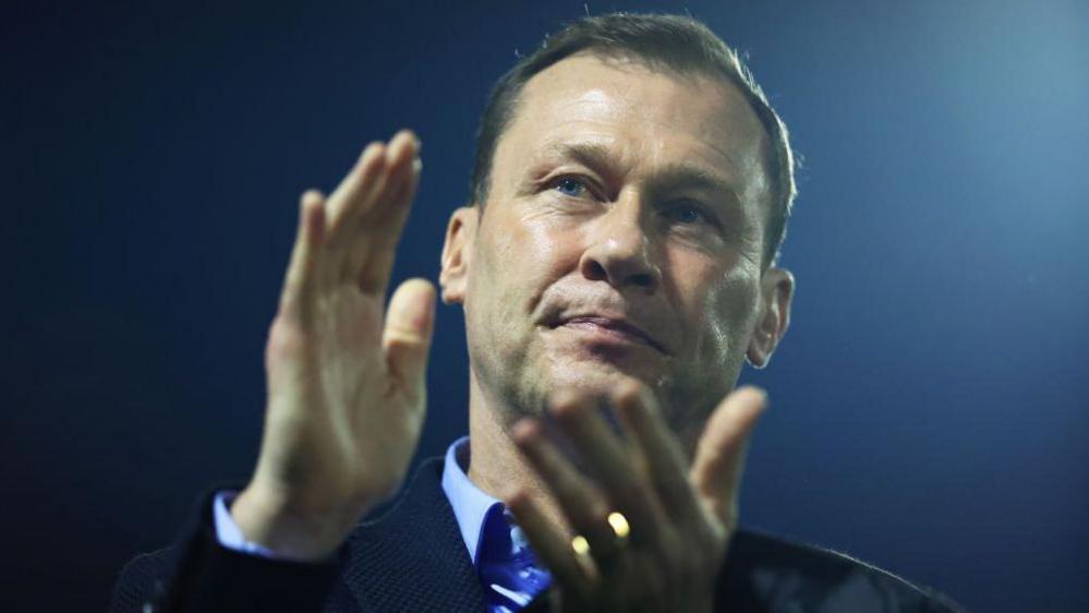 Duncan Ferguson claps his hands. It is night-time and a football stadium floodlight glows behind him.