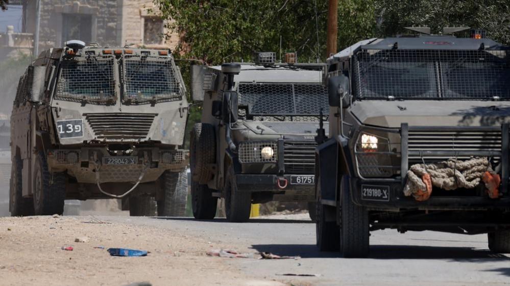Three armoured Israeli miltiary vehicles drive on a road in Jenin