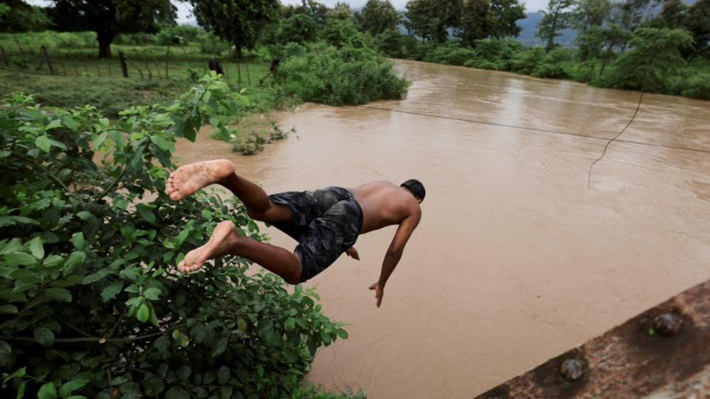 A man can be seen diving head first into the brown waters of a river that has burst its banks in El Progreso, Honduras