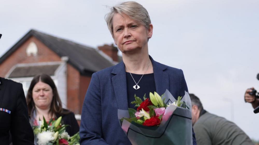 Yvette Cooper walks holding a bouquet of flowers