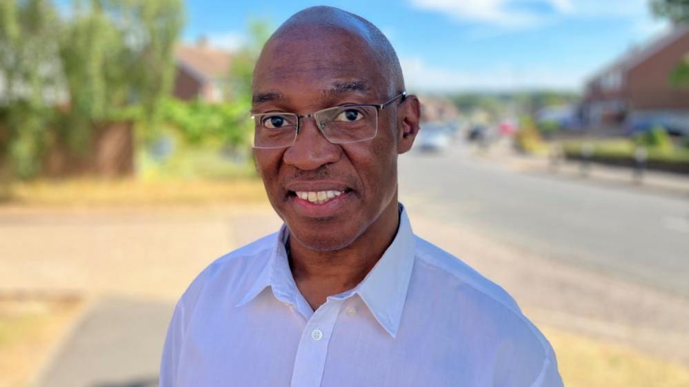 Montell Nefville, looking at the camera, wearing a white shirt and glasses
