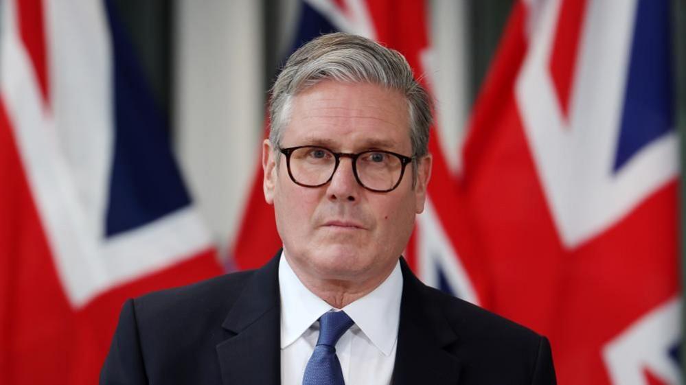 Prime Minister Sir Keir Starmer standing in front of two union flags