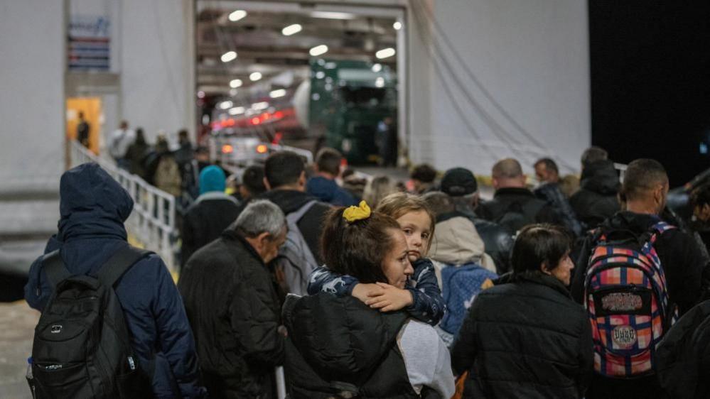 A large crowd of people enter a ferry