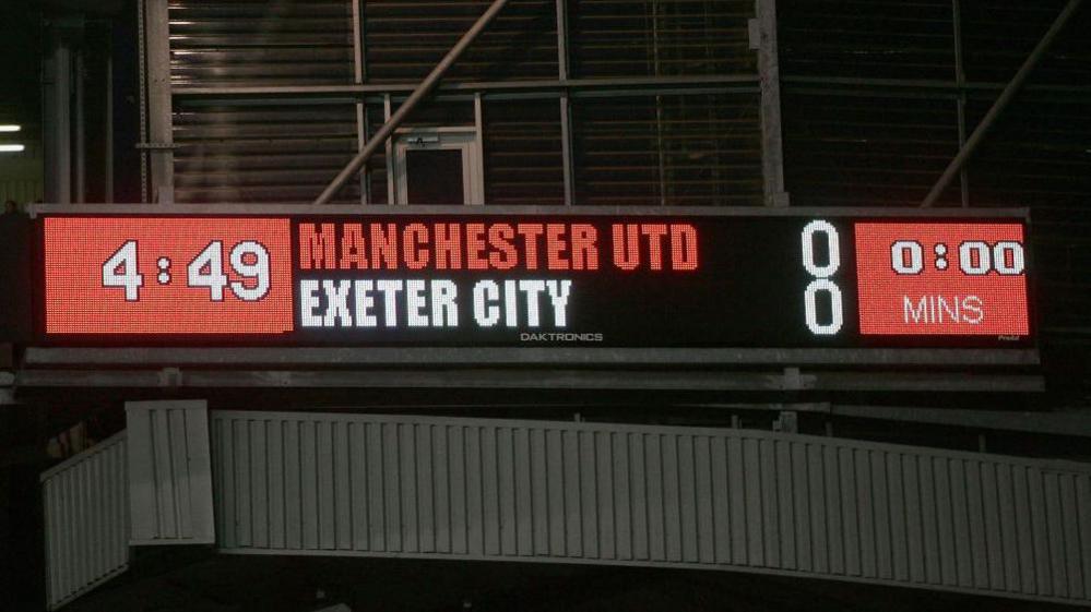 Old Trafford scoreboard showing 0-0 draw between Exeter City and Manchester United 