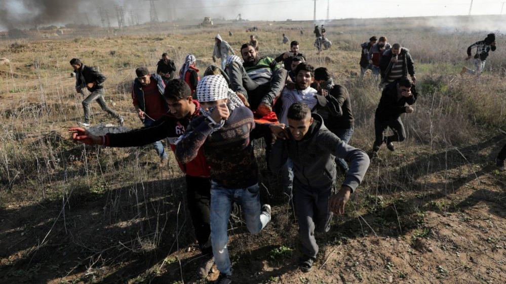 Palestinians carry a wounded protester during clashes along the border between Israel and east Gaza, 8 December 2017