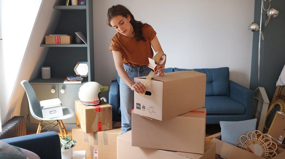 Woman packs boxes in room with shelves and sofa in background