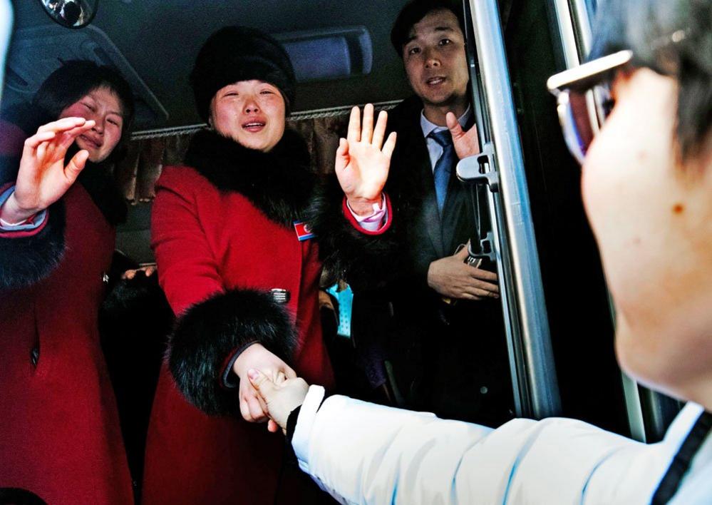 North Korean hockey players stand on a bus and wave farewell