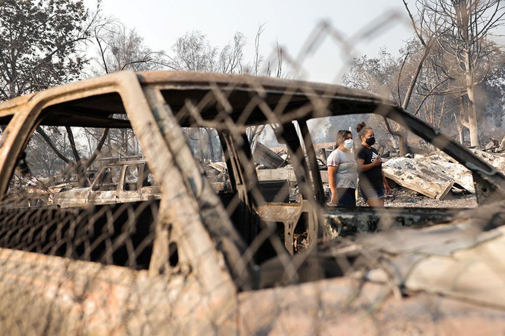 People walk behind off a burned car after wildfires destroyed an area of Phoenix, Oregon