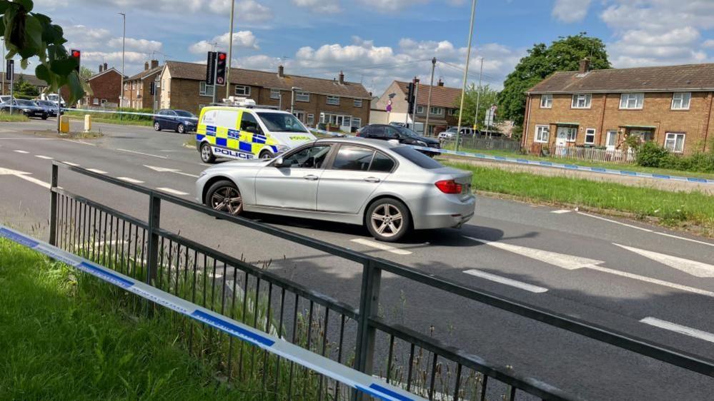 Queens Road closed with a silver car in the foreground and a police car in the background