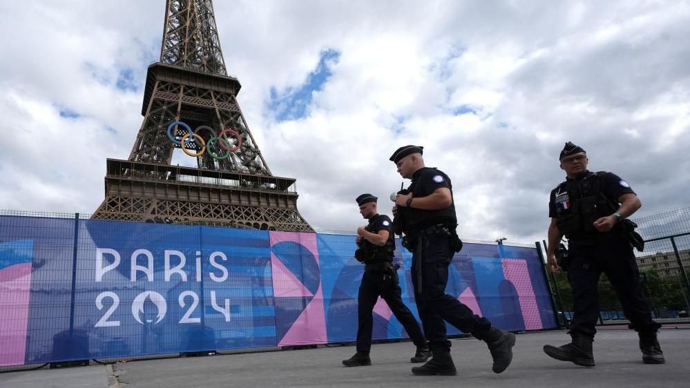 Police officers walk in front of the Eiffel Tower in Paris. The Olympic rings can be seen mounted half way up the tower.