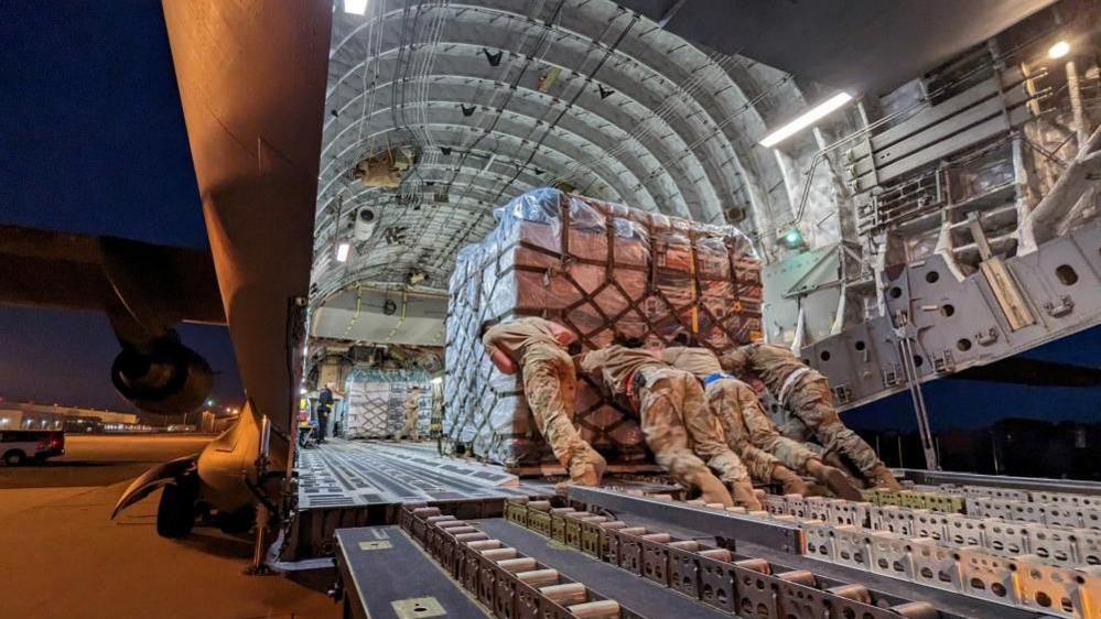 Military personnel loading equipment onto the back of a plane