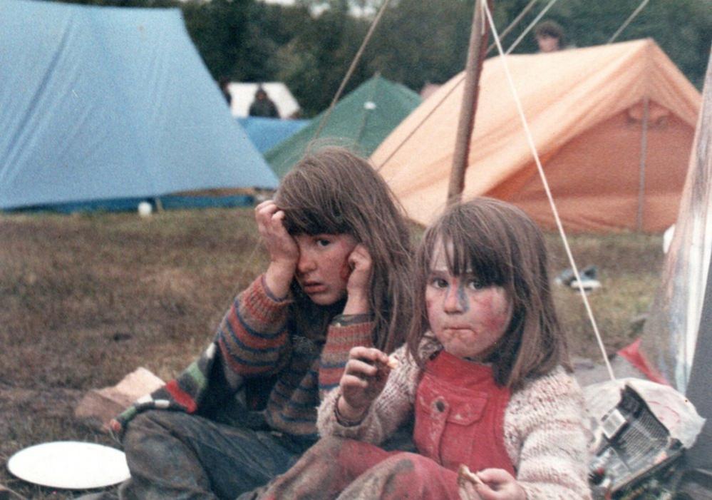 Two children sitting on the ground with tents behind them