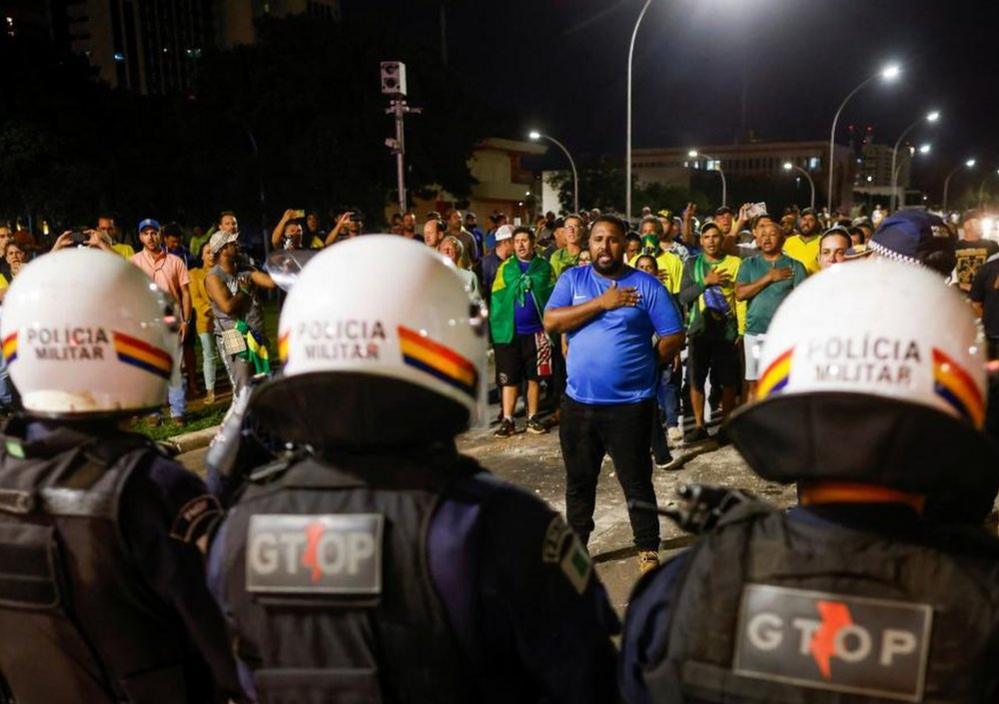 Police officers stand guard as supporters of Brazil's President Jair Bolsonaro gesture during a protest after supreme court justice Alexandre de Moraes ordered a temporary arrest warrant of indigenous leader Jose Acacio Serere Xavante for alleged anti-democratic acts, in Brasilia, Brazil, December 12, 2022