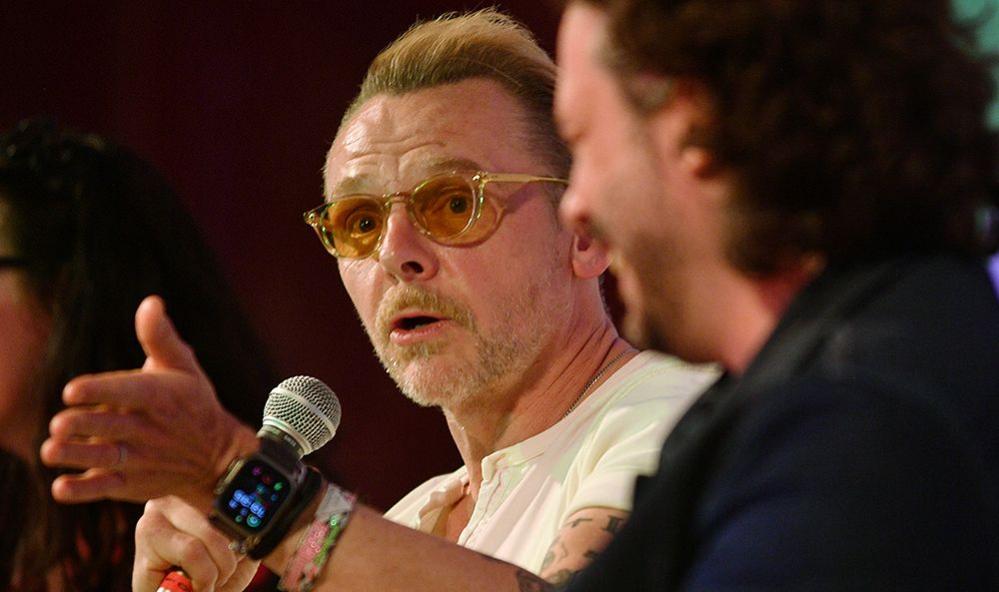 Simon Pegg gestures while speaking into a microphone onstage with Edgar Wright during a 20th anniversary screening and Q&A of Shaun of the Dead at Glastonbury Festival in June 2024