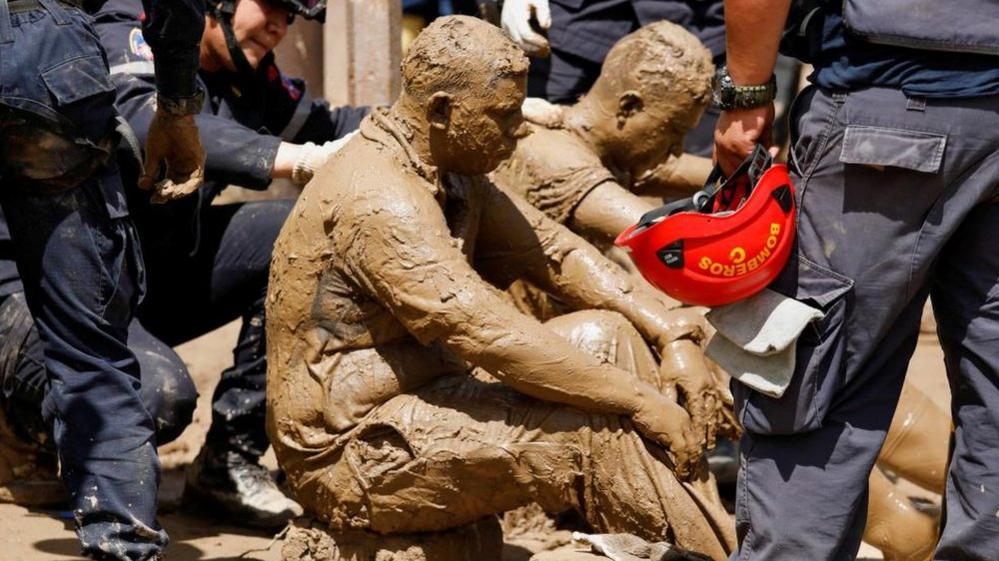 Volunteer rescuers who were attacked by wasps while removing debris to recover the body of a person are attended by firefighters, as the search of missing persons who were swept away on Saturday by devastating floods following heavy rain continues, in Las Tejerias, Aragua state