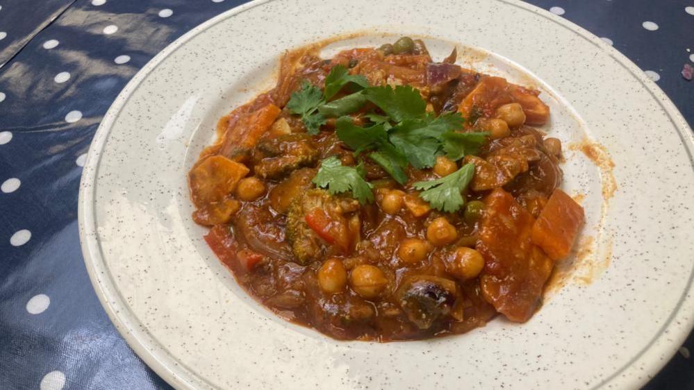 A plate full of chicken and chickpea curry in a white speckled bowl, with fresh coriander on the top .