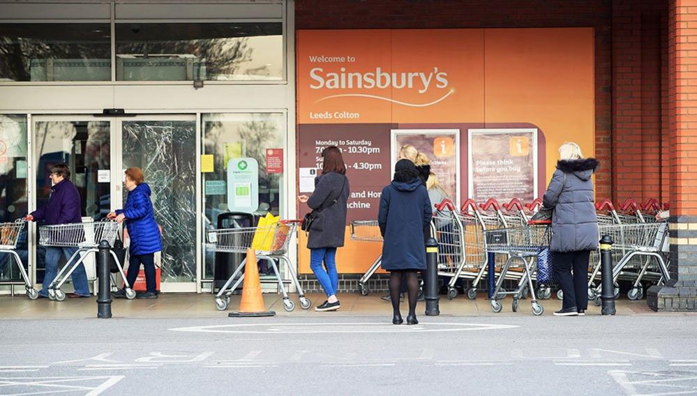 People observe social distancing while queuing at a Sainsbury's supermarket at Colton, on the outskirts of Leeds