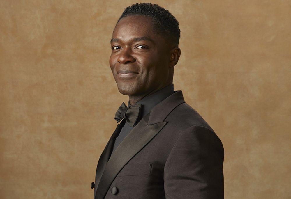 David Oyelowo at the Golden Globes, pictured in a tuxedo with a black bowtie against an orange background