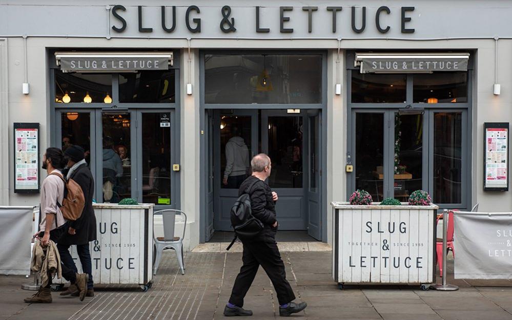 A general view of a Slug and Lettuce bar and restaurant pub in the High Street on February 18, 2023 in Colchester, England. People with backpakcs are seen walking in front of the pub along the street.