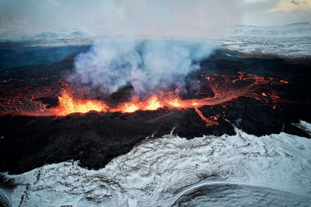 An aerial view taken with a drone shows lava and smoke spewing from a volcanic fissure during an eruption, near the town of Grindavik, in the Reykjanes peninsula, southwestern Iceland, 19 December 2023. The Icelandic Meteorological Office (IMO) announced the start of a volcanic fissure eruption near the Sundhnuka crater, north-east of Grindavik, on the night of 18 December, following weeks of intense earthquake activity in the area. The power and seismic activity of the eruption have decreased over time, IMO reported on 19 December, adding that since the eruption began, about 320 earthquakes have been recorded.