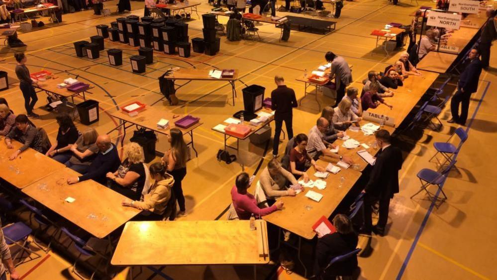 People sitting around tables in a sports hall