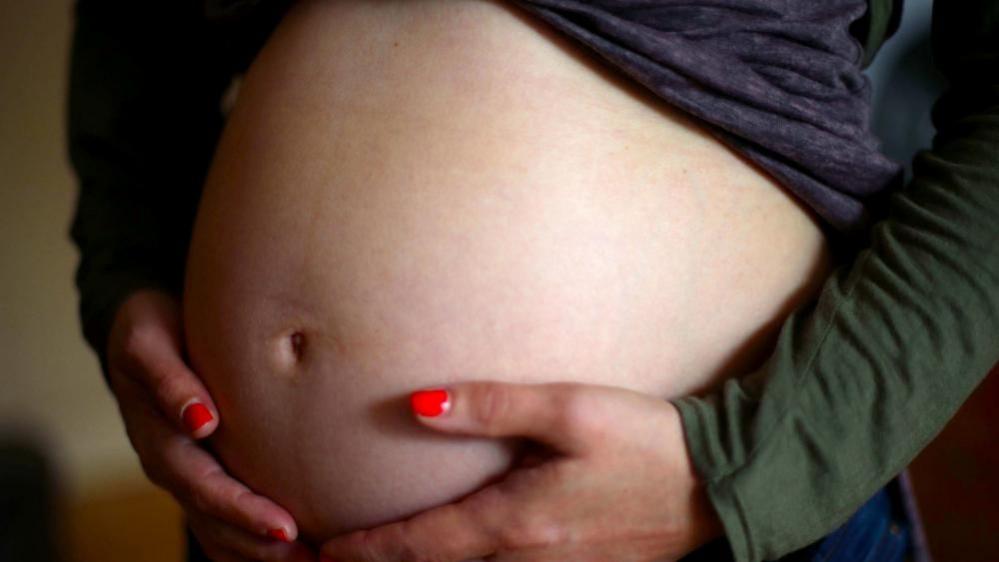 Pregnant woman wearing red nail varnish holding stomach