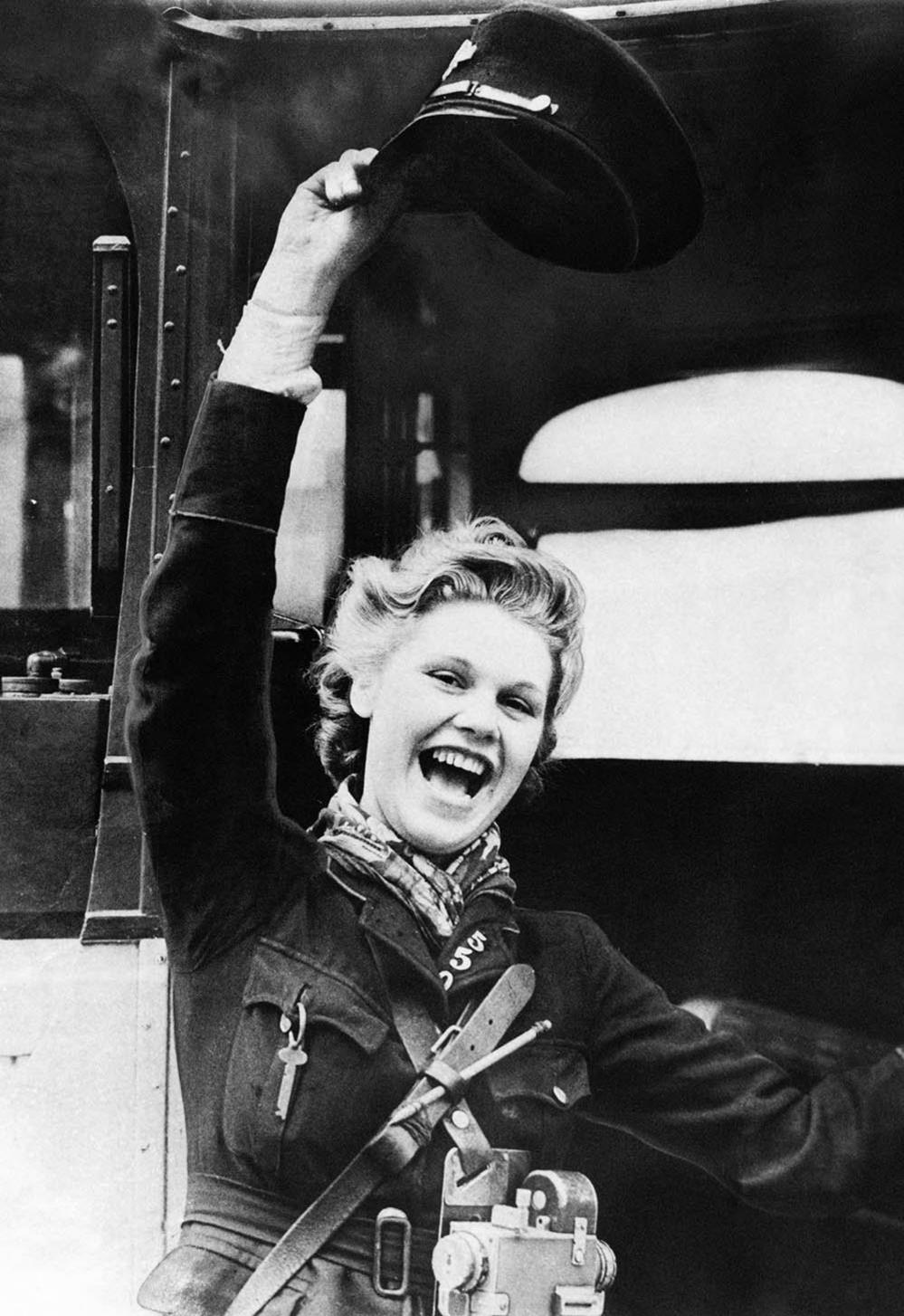 A woman bus conductor waves her hat in celebration