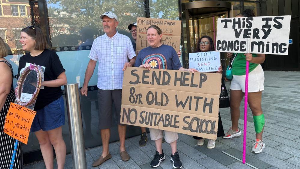 Parents with placards standing outside office building