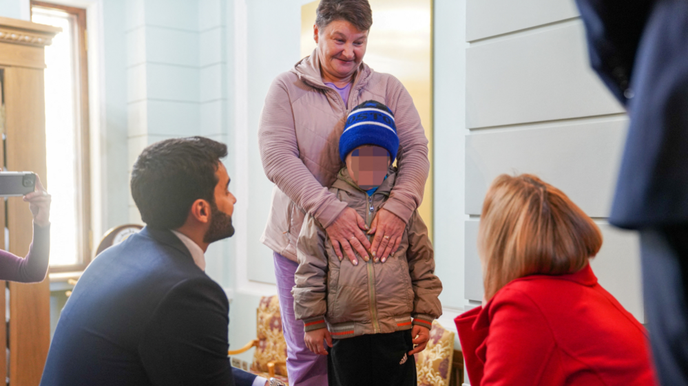 Woman embracing boy, talking to two kneeling officials