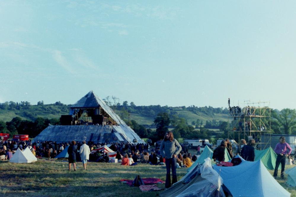 Festival-goers outdoors and a stage in the distance