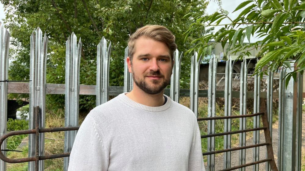 Man with light brown hair and short beard stands in front of closed-off footpath