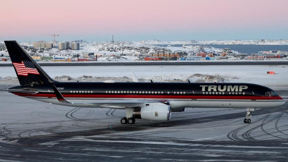 A red, white and blue plane with 'Trump' written on it is parked on a snowy runway.