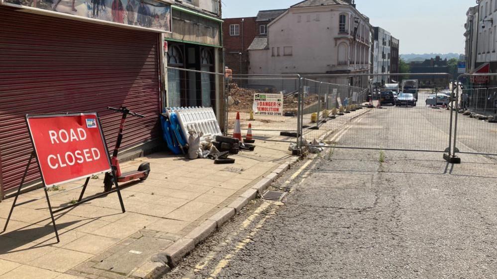 Road closed sign in front of metal fencing on a street