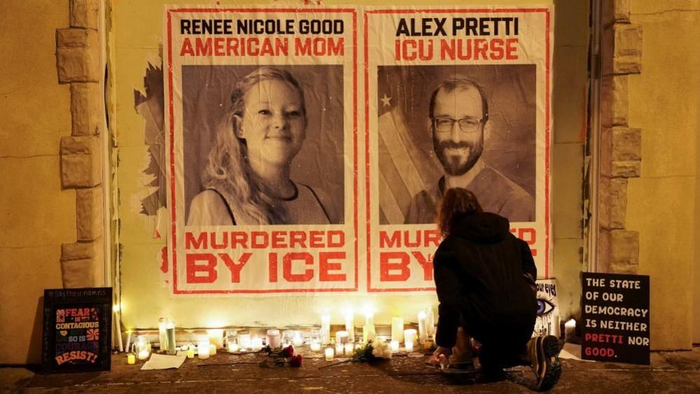 Posters of Alex Pretti and Renee Good's faces, saying "Murdered by ICE", with candles placed on the ground