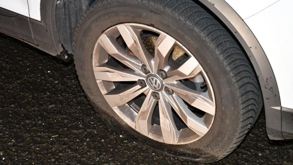A close up shot shows a tyre of a white Volkswagen clearly flat. 