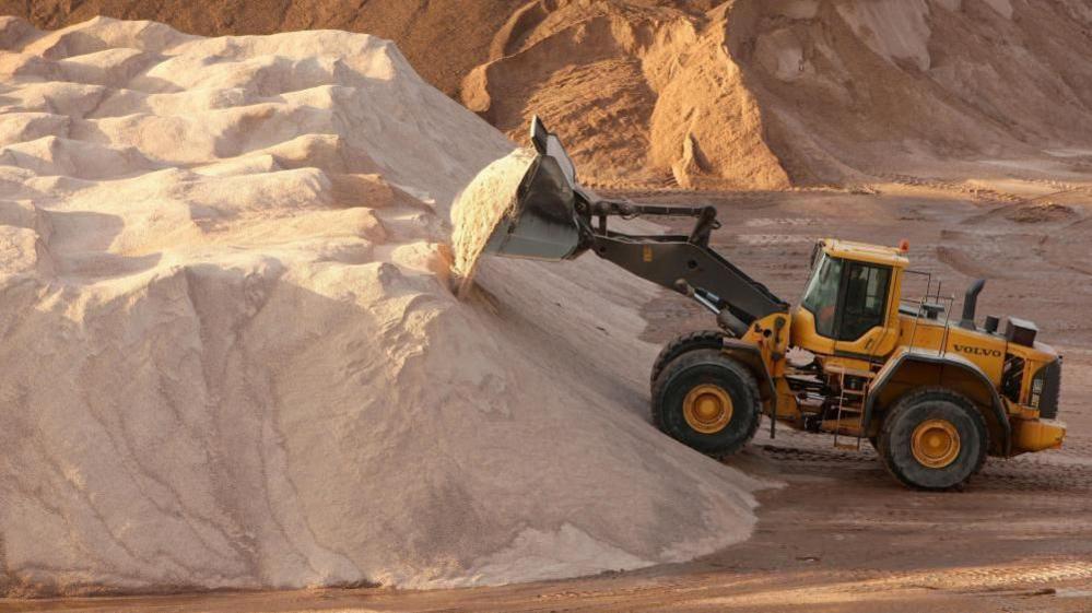 A truck at Winsford Salt Mine gathers rock salt to be used on the country's roads during freezing weather. A huge pile of rock salt can be seen, with more seen in the background.