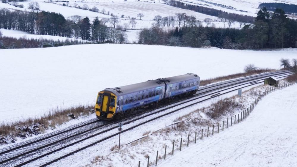 A blue and yellow ScotRail train on the tracks in snowy conditions near Gleneagles in Perthshire.