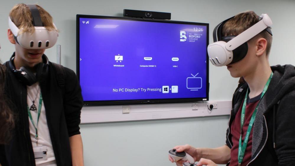 Two students wearing virtual reality headsets with an interactive TV behind them