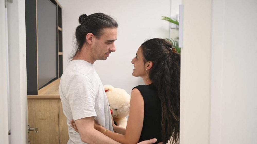 Ariel Cunho wearing a white T-shirt looks into the eyes of his girlfriend as both hold each-other in profile