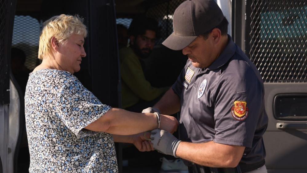 A law enforcement officer puts handcuffs on a woman's wrists